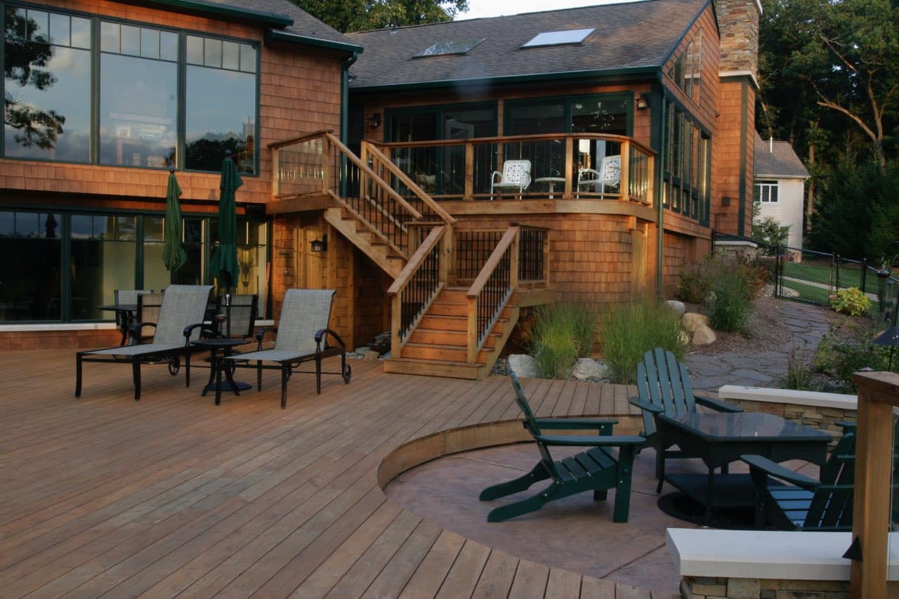 As Grand Rapids Deck Builders, Precision projects are unique to each homeowner. A deck, sunroom, and fire pit combination extending the back of a house.