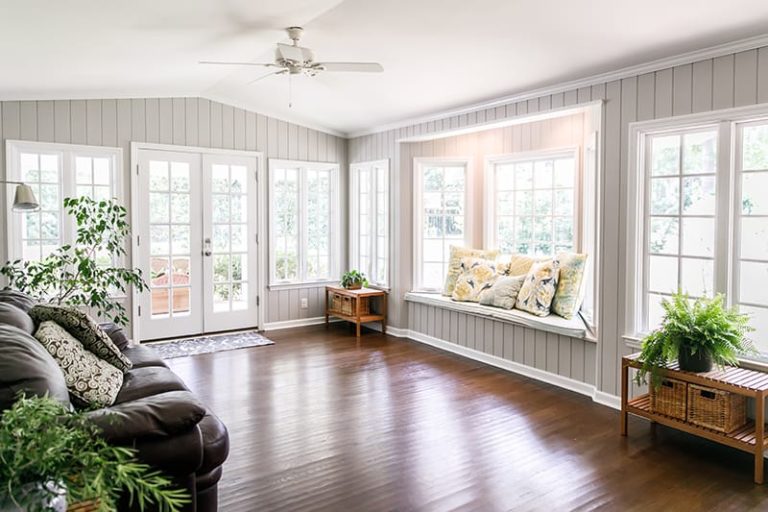 What's the Difference Between a Sunroom and an Enclosed Patio? A patio is something originally outside that makes you feel like you're inside, while a sunroom is a building add-on that makes you feel like you're outside. A sunlit sunroom with dark hardwood flooring.