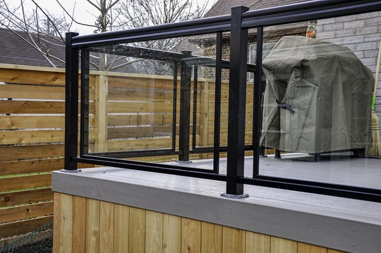 Glass panels along railings are just one example of outdoor deck decor that you can add to a Precision Decks project. Glass sits framed inside a black mounted railing.
