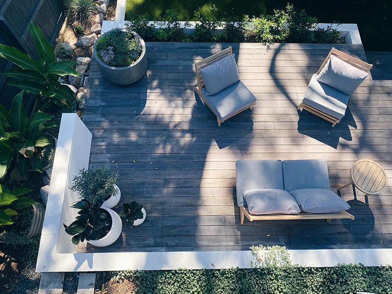 A backyard entertainment area with an elevated deck, couch, two chairs, and plants, shot from above..