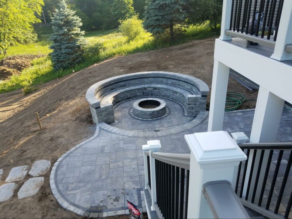 Photo of an elevated deck with steps leading down to a curved paver patio with a built-in curved seating area.