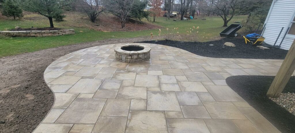 Photo of a curved patio with natural stone pavers and a stone fire pit situated in the center.