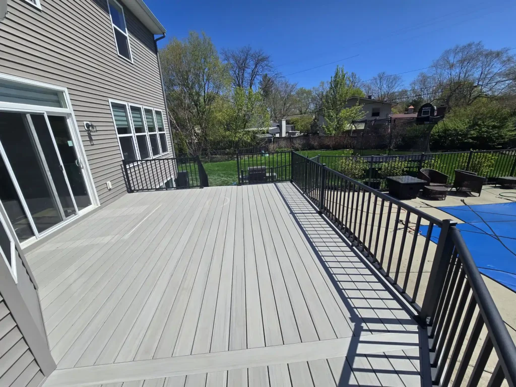 Spacious AZEK deck with black railings overlooking a backyard pool.