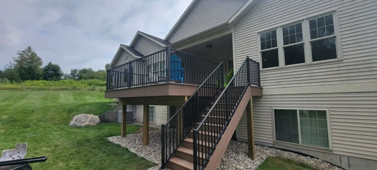 Photo of elevated brown deck with black railings, staircase, and pebble landscaping underneath.