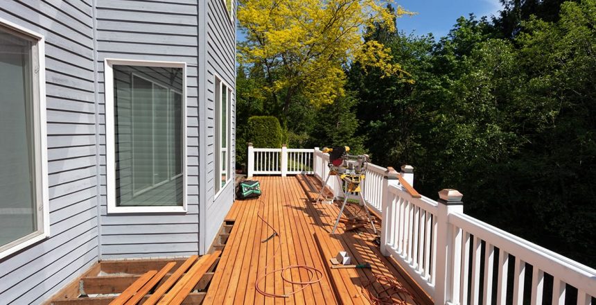 A deck repair in progress. New wood planks being installed on an elevated wrap around deck with white guard rail.